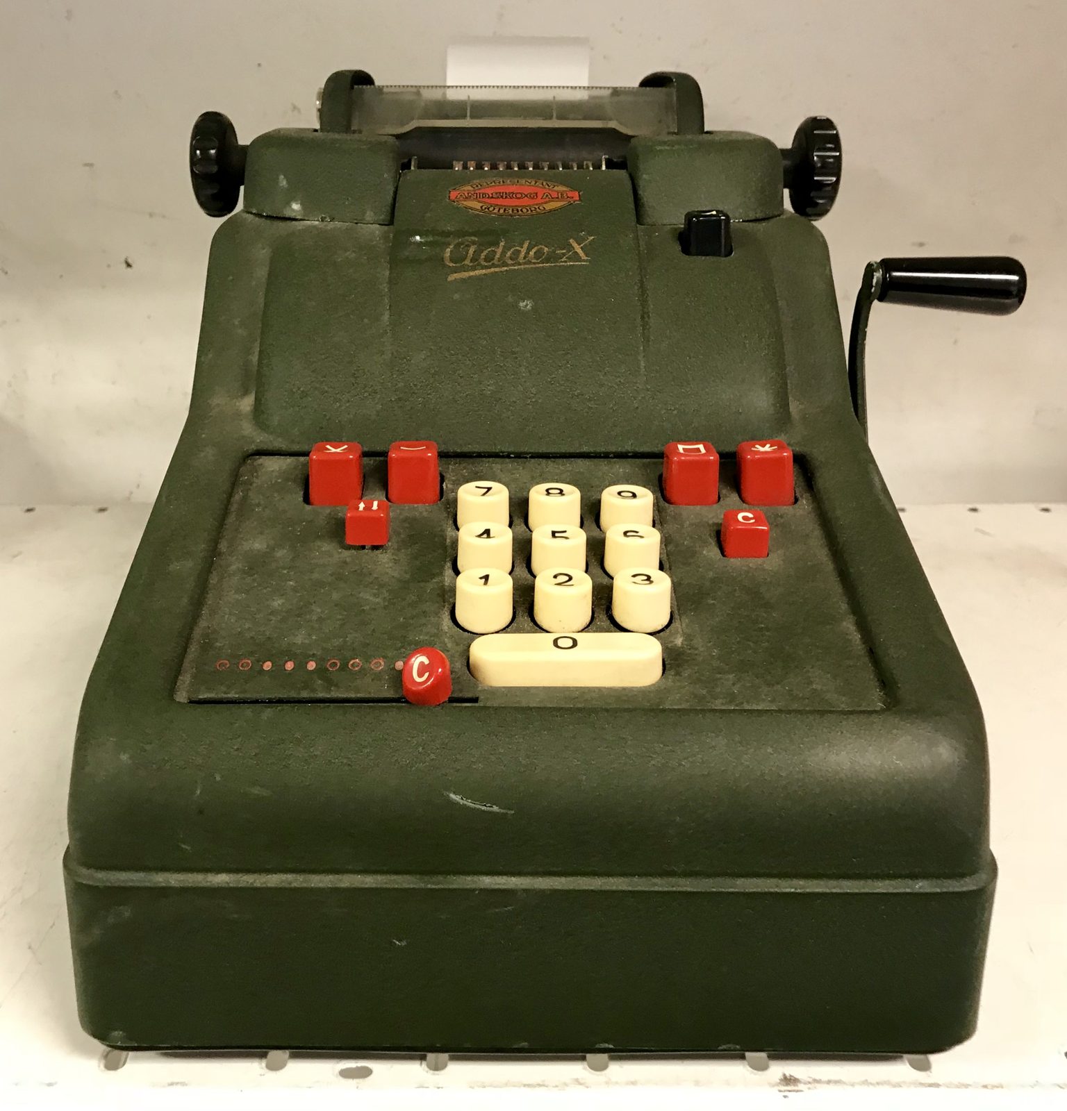 A green adding machine with a paper tape and number keys