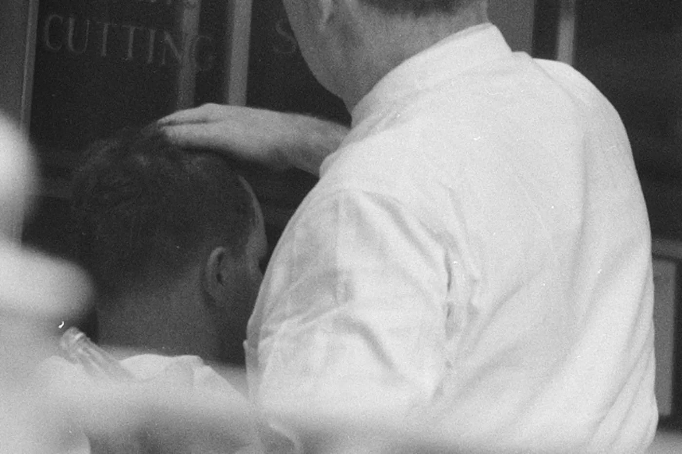 A barber cutting a guest's hair in front of a hair cutting sign.