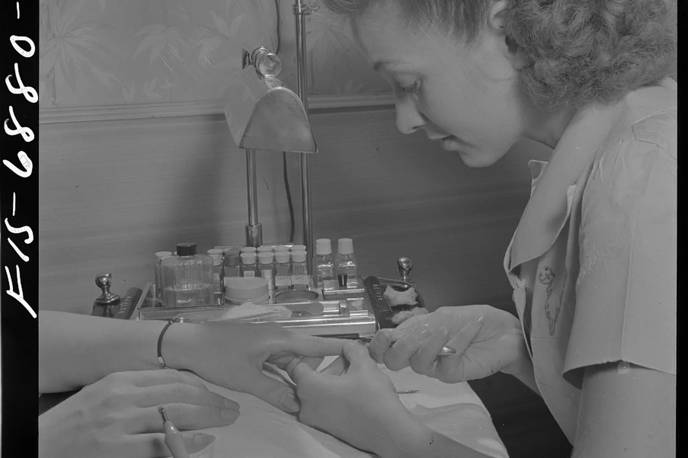 A manicurist working on a guest's hand at a small work table.