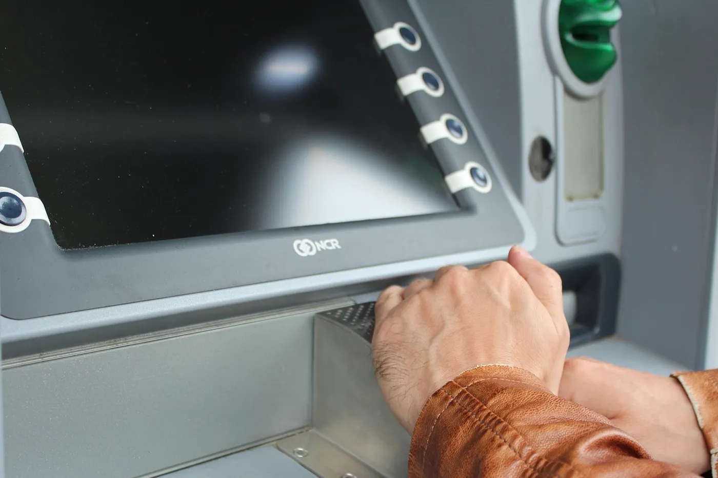 Hands resting at a bank machine, with the screen dark beside the keypad.