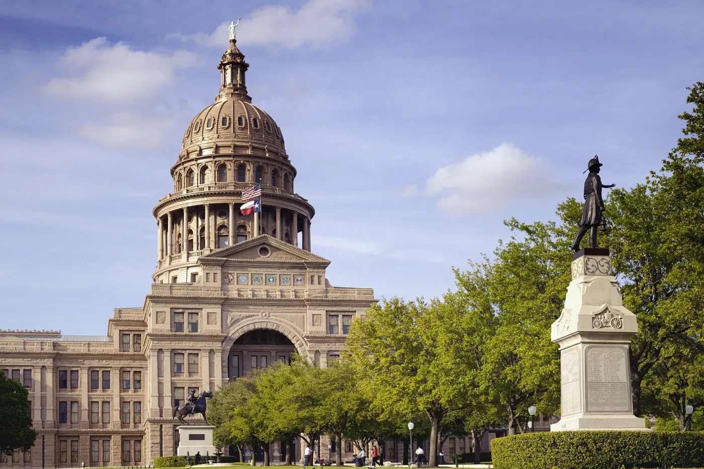 The Texas capitol dome in daylight, with the flags along the walk.