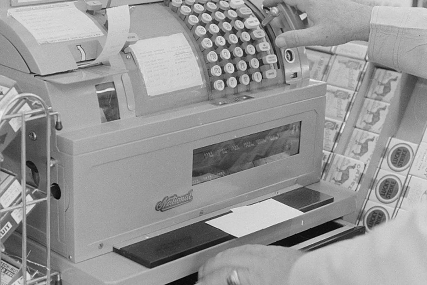 Hands on a cash register, with a receipt tape and a total in the window.