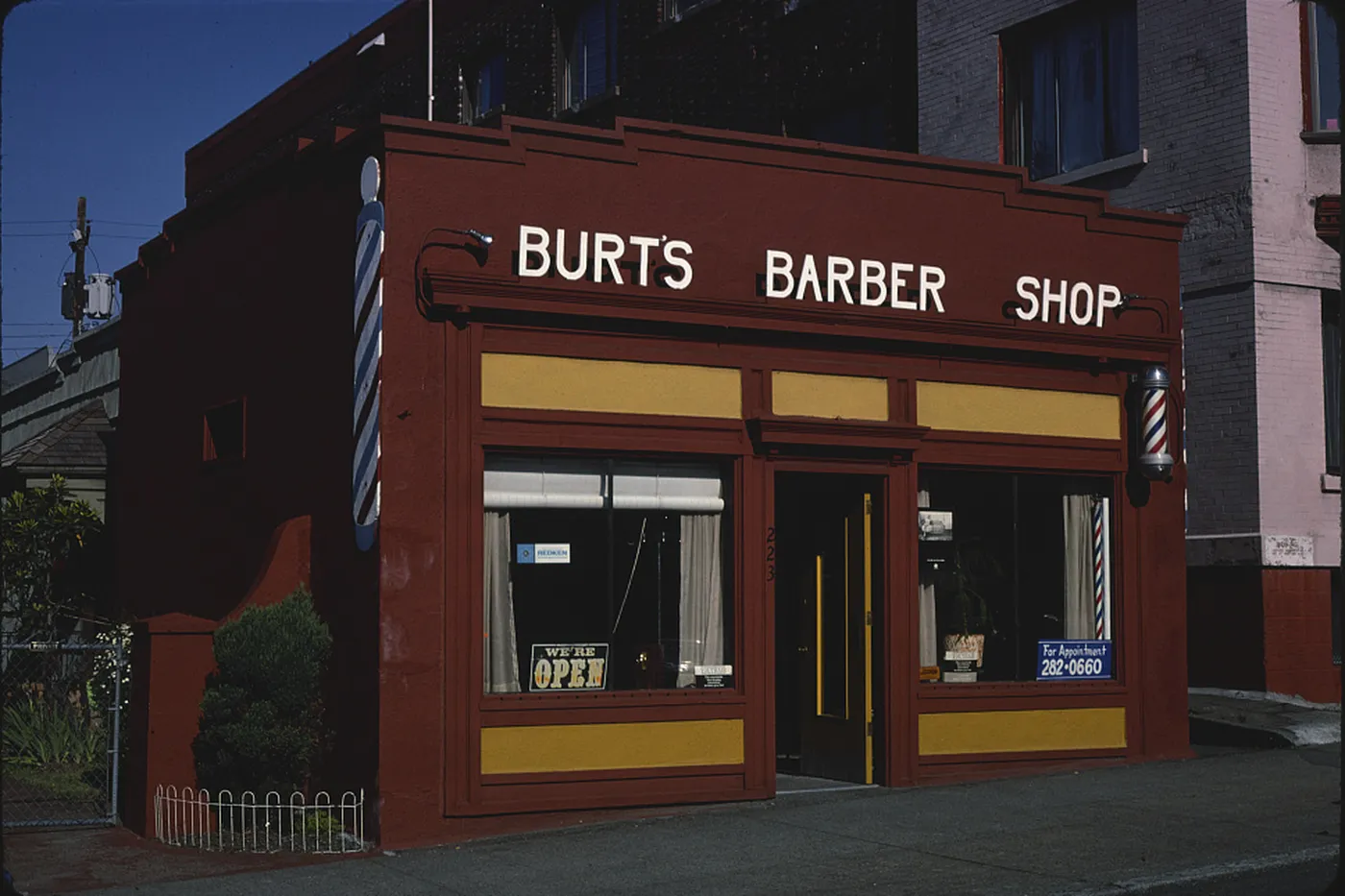 The front of a barber shop, with the door open and a pole on the wall.
