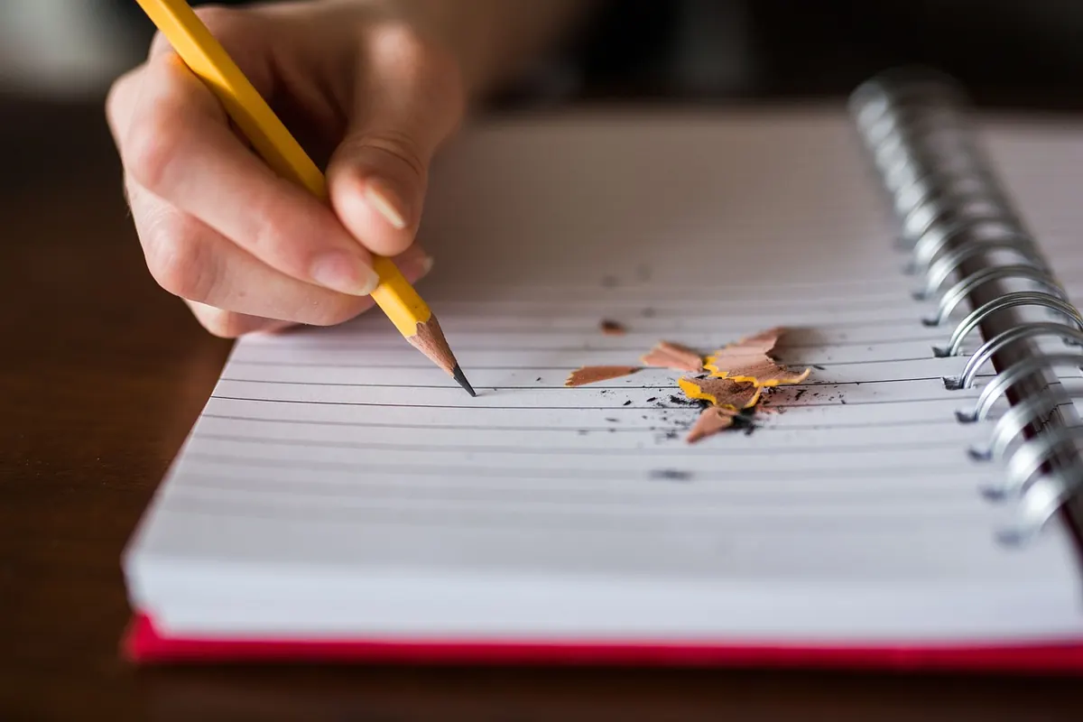 A hand holding a pencil over a lined notebook