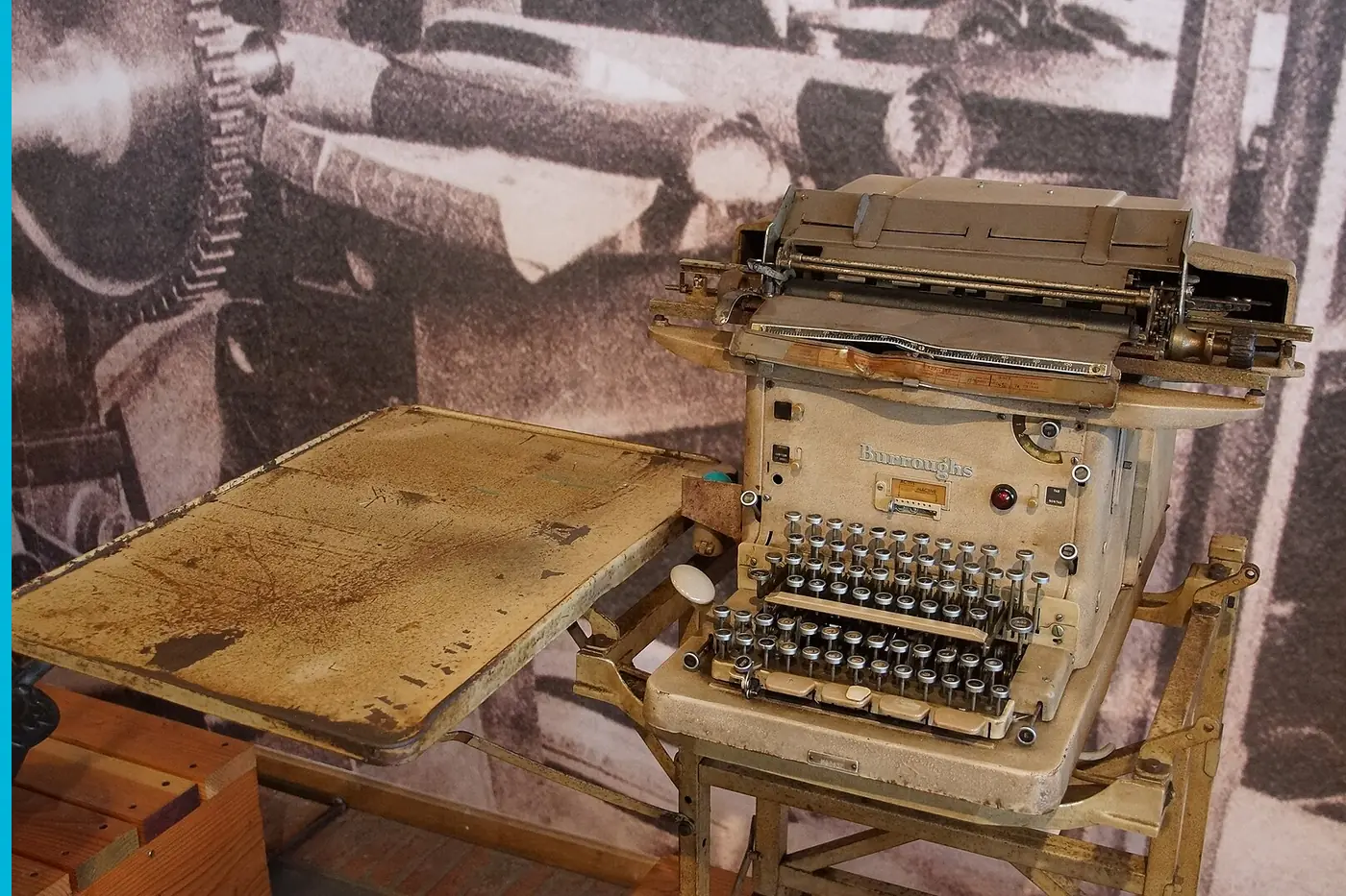 An adding machine on a wooden desk, another machine beside it