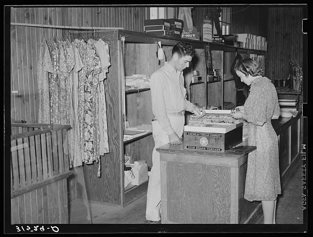 Two women sort goods and papers at a store counter.