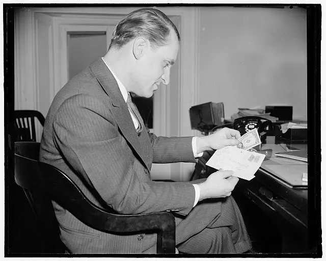 A man at an office table reads a stack of papers.