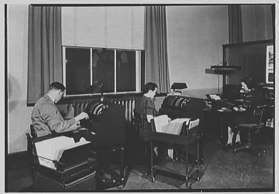 Three people run bookkeeping machines in an office.
