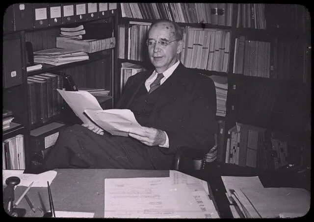 A man sits with papers in front of shelves of books.