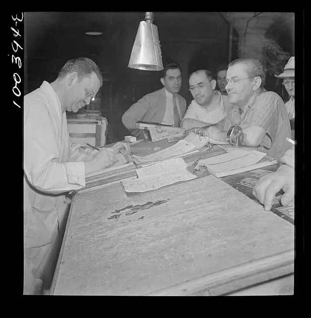 Men work through papers together at a warehouse table.