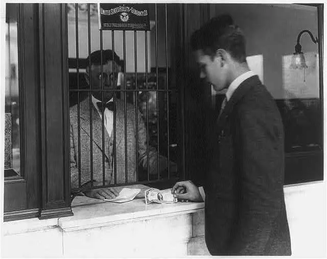 A man at a bank window hands paper across the counter.