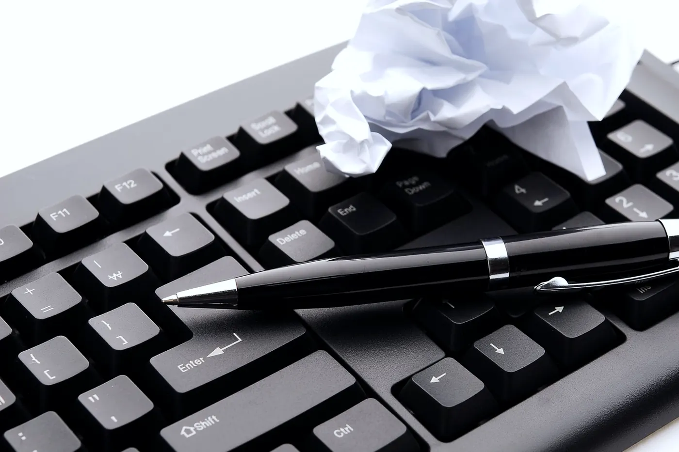 A keyboard, a pen, and a crumpled sheet of paper