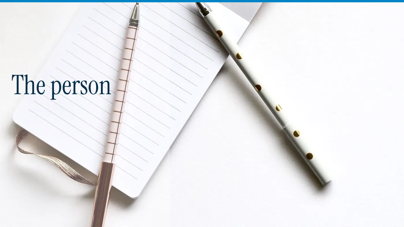 A blank notebook and two pens on a white table, with the words The person in large type
