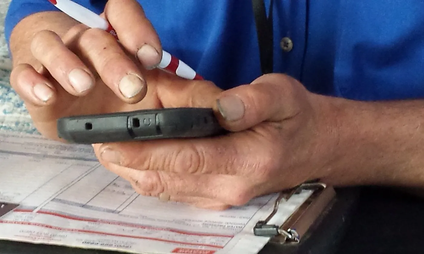A tradesman's hands holding a phone over a work order