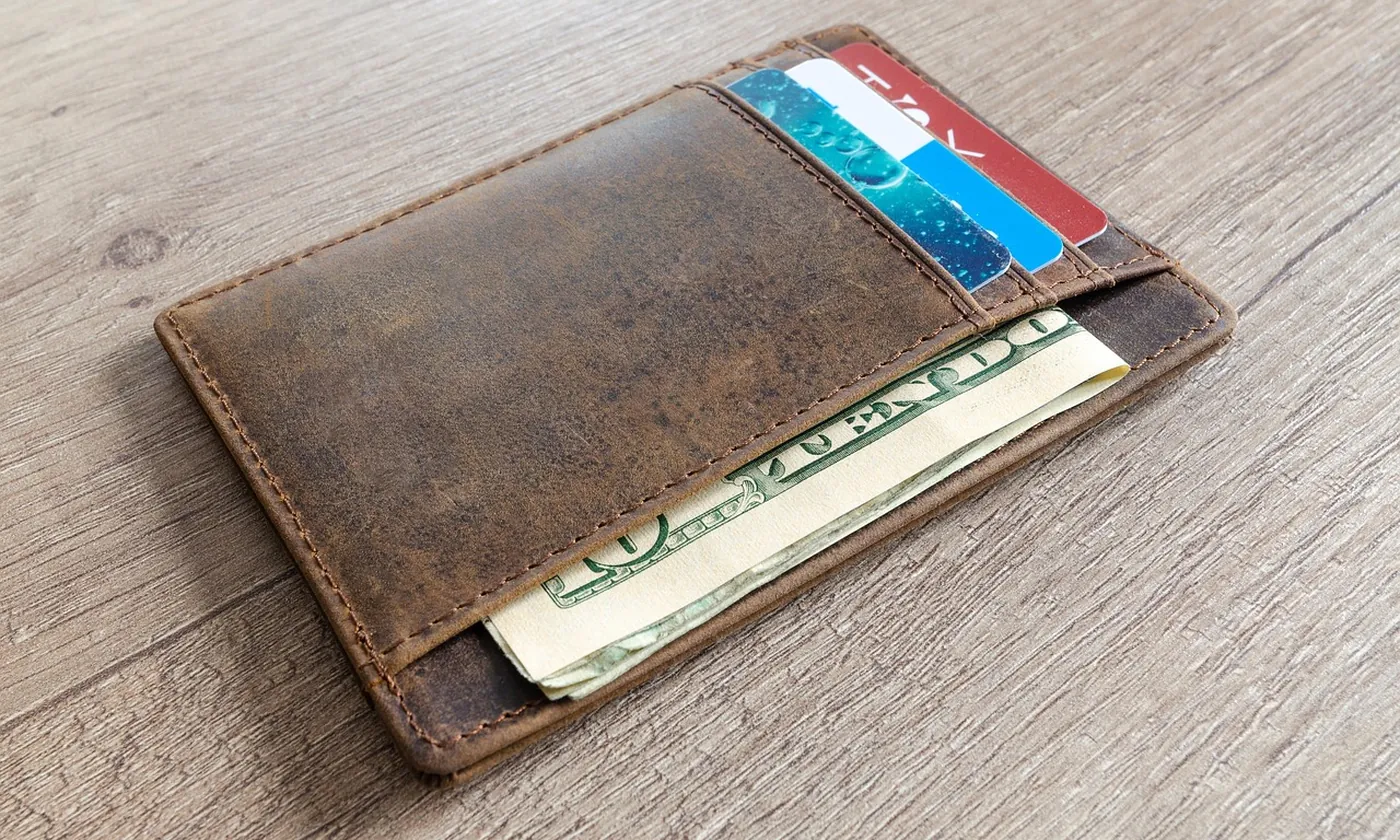 A leather card wallet holding two cards and folded bills on a wooden table
