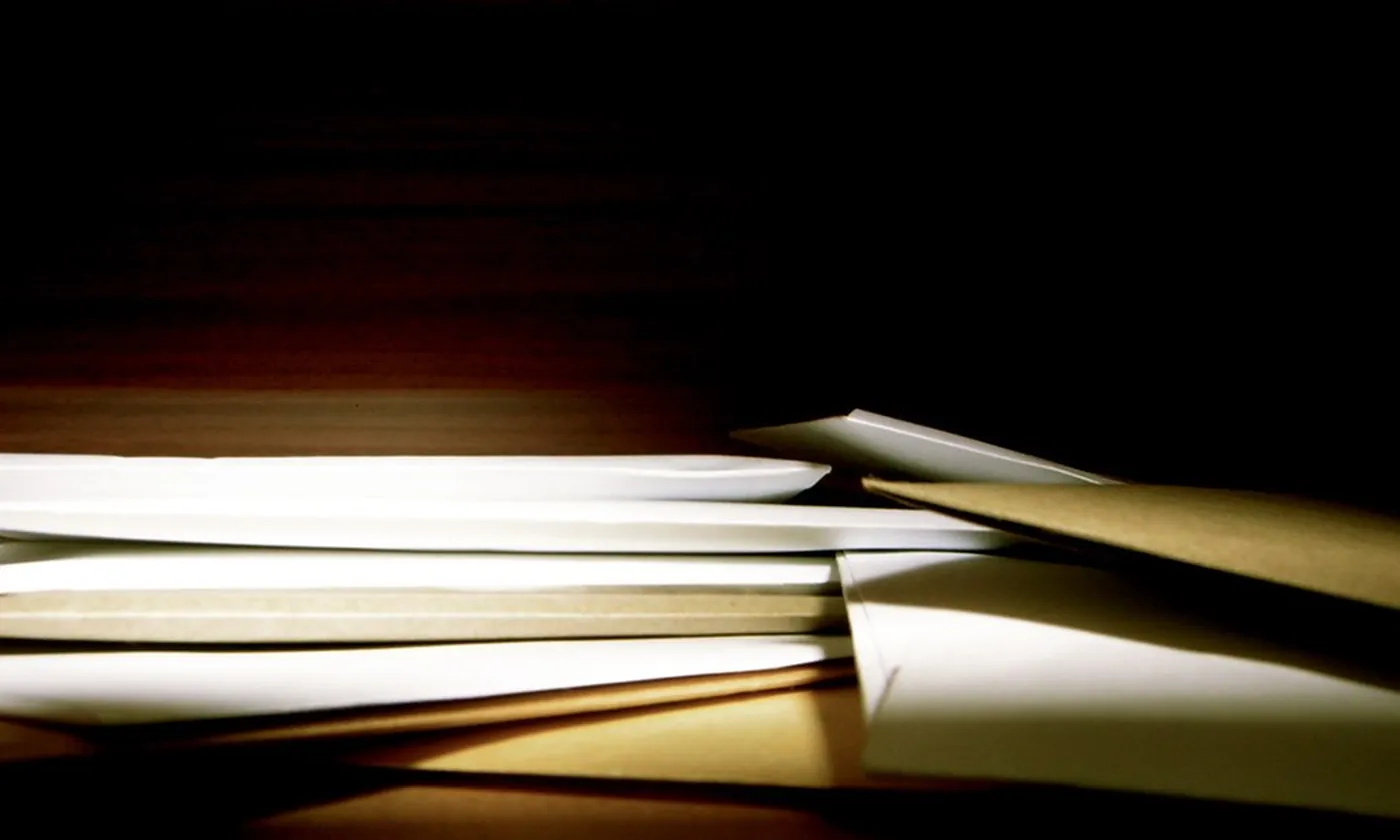 A stack of envelopes catching a strip of light on a dark table