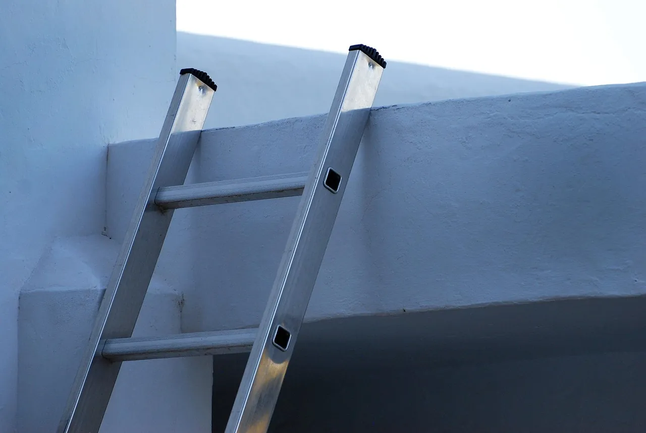 An aluminum ladder against a white wall