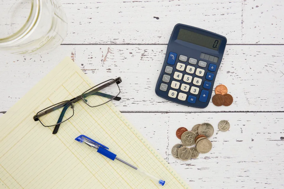 A calculator, coins, and a ledger sheet on a table
