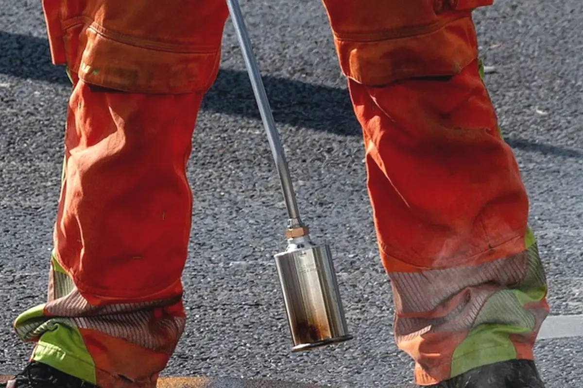 A worker holding a torch over a pavement joint