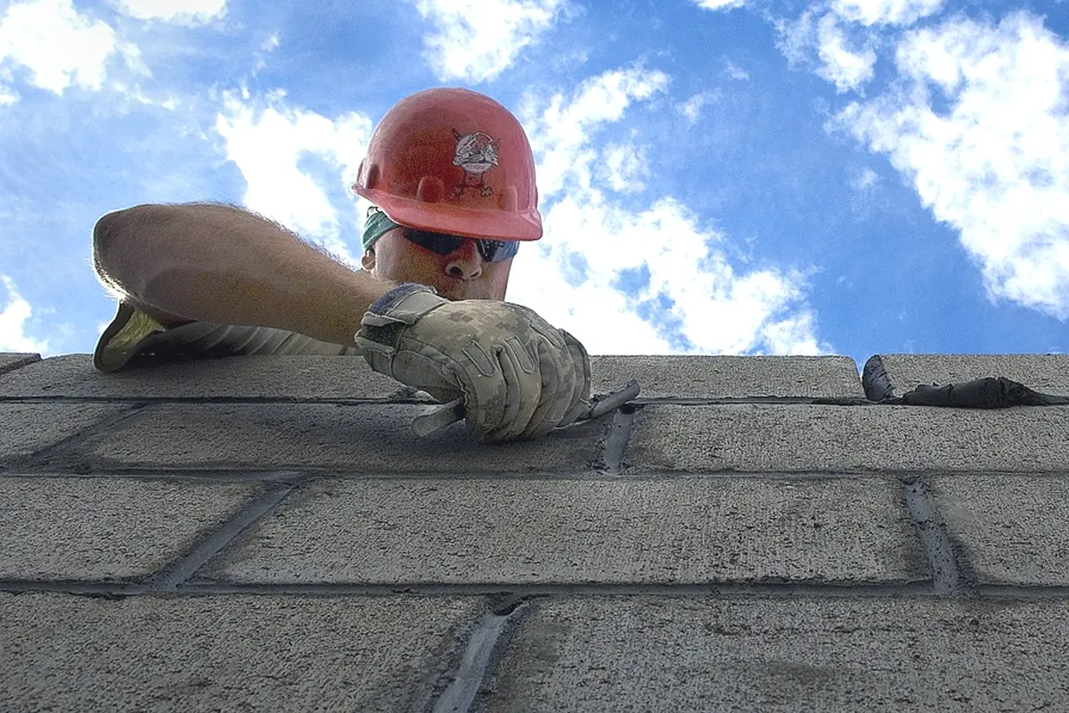 A mason in a hard hat setting the next block