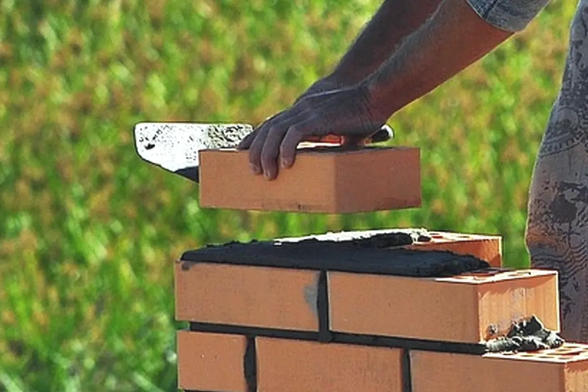 Hands setting a brick into a fresh course
