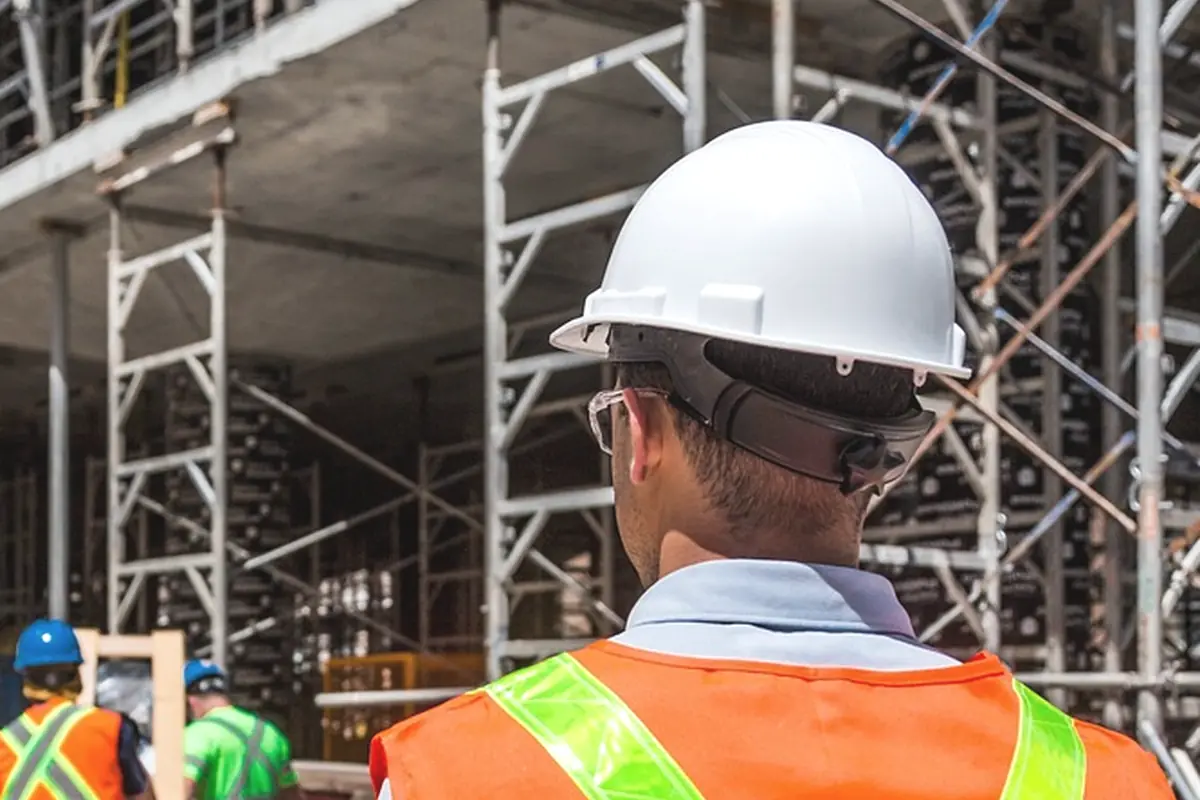 A worker in an orange vest facing a scaffolded frame