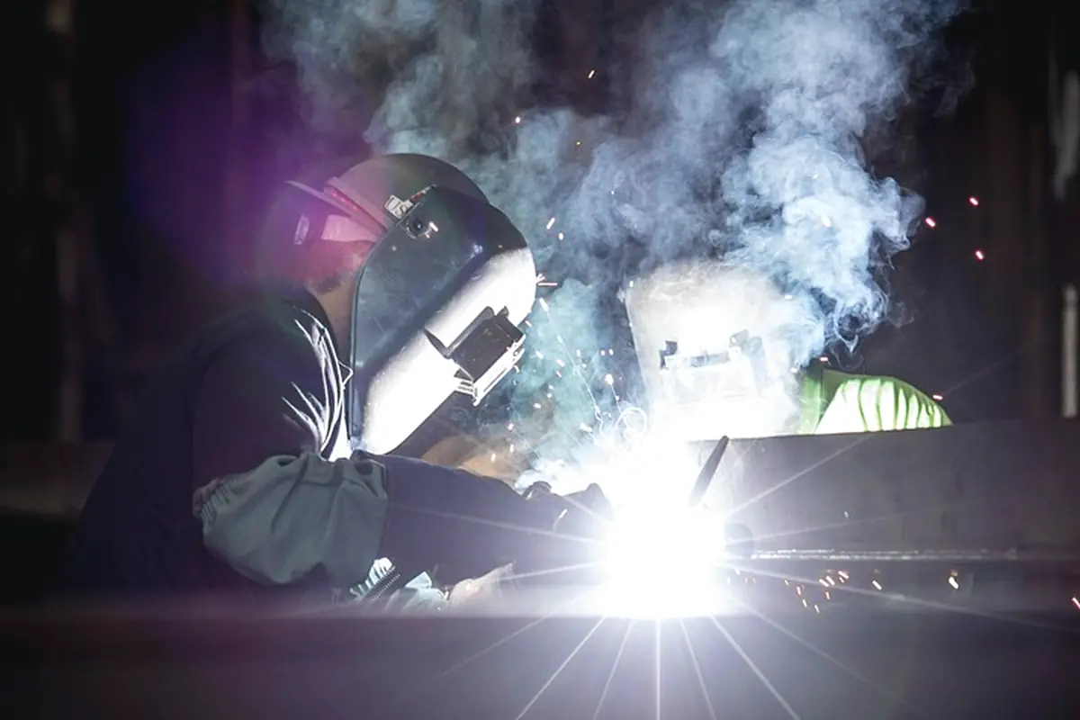 A welder in a helmet working a steel joint