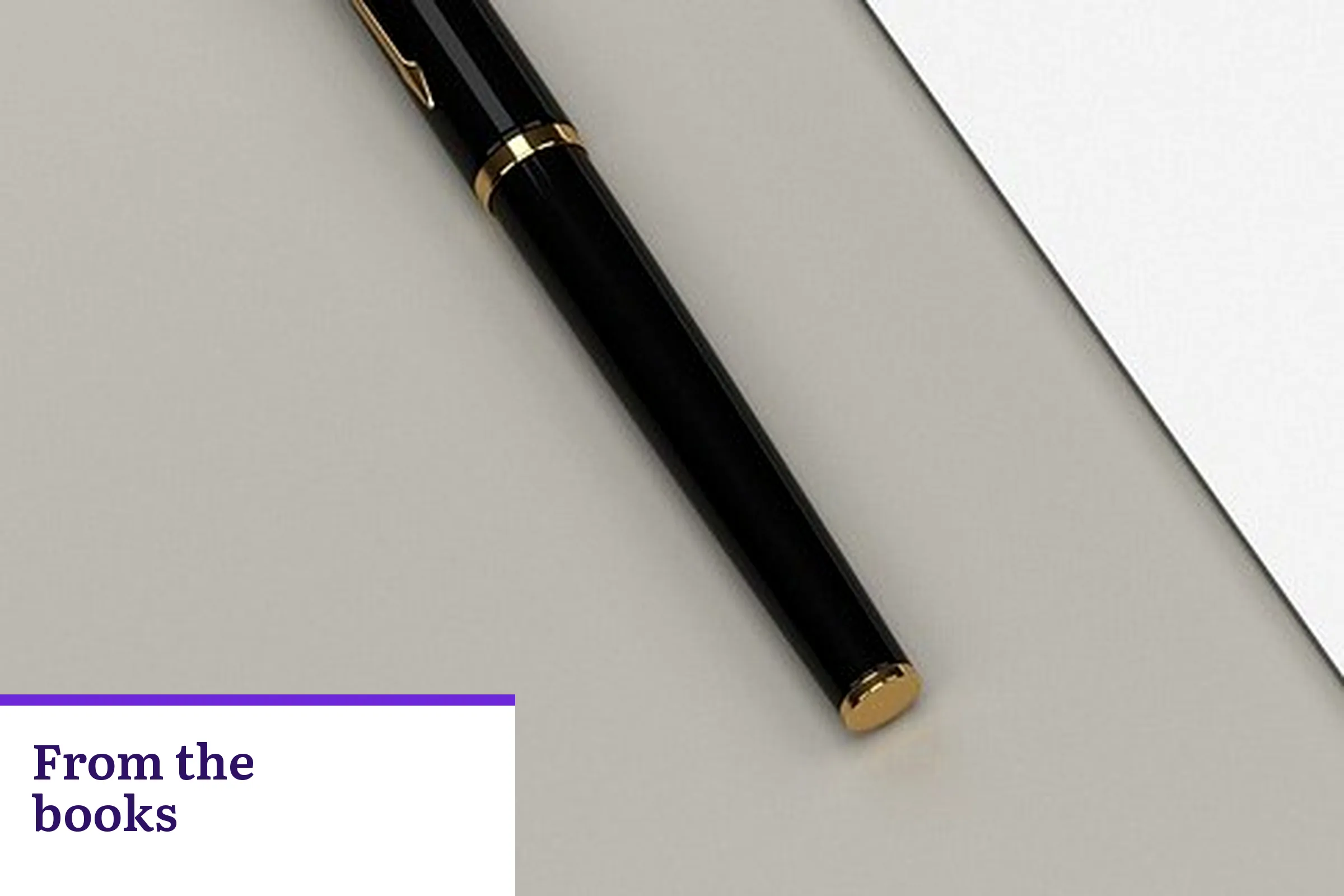 A black pen with a gold band on a gray surface, with the words From the books