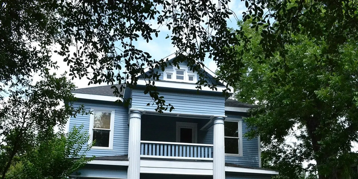 Blue house and columned balcony under live oaks