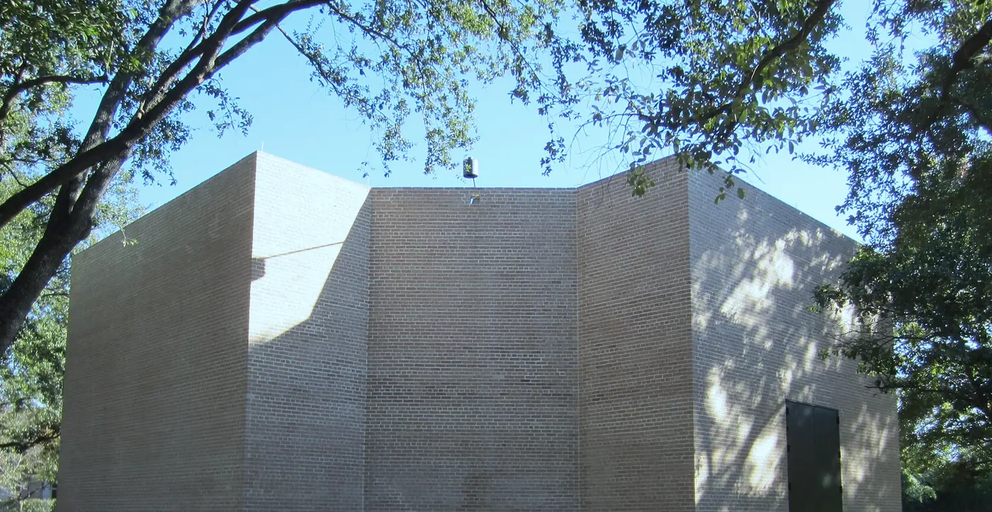 A brick chapel under live oaks, cropped above the sign