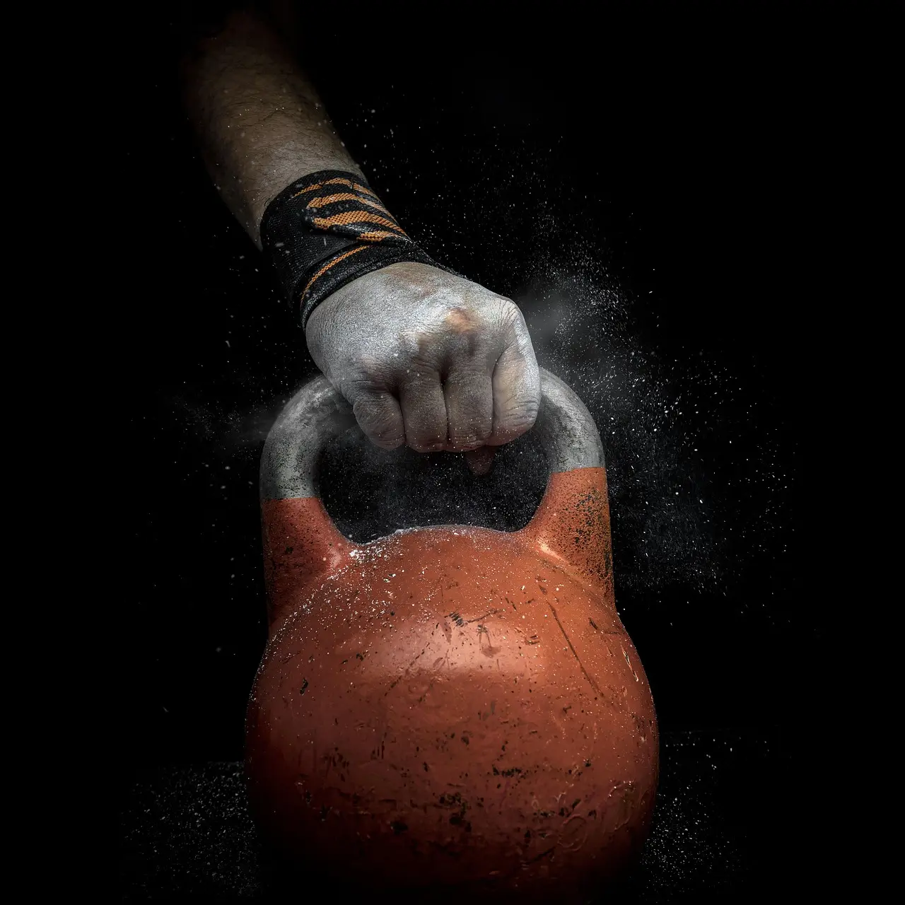 A chalked hand gripping an orange kettlebell on a dark ground.