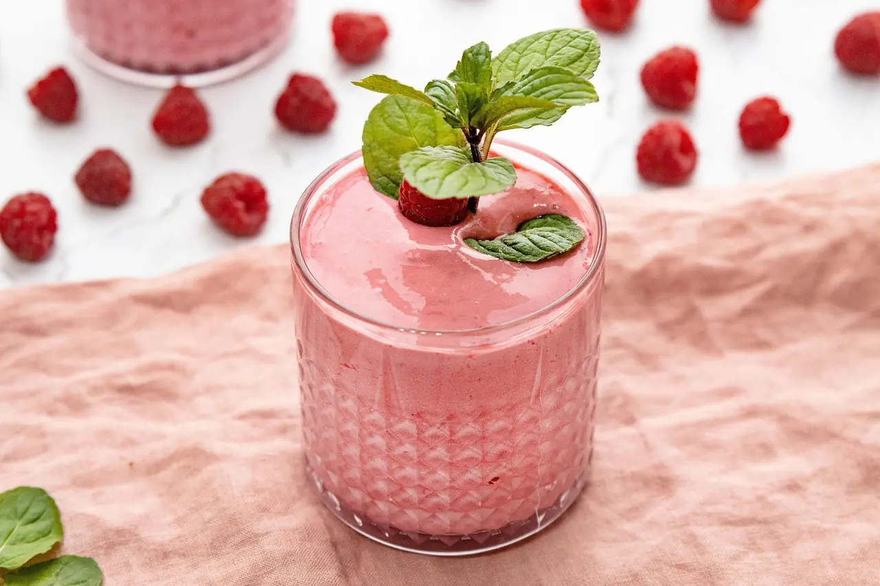 A pink berry smoothie in a clear glass, with mint on top and no label.