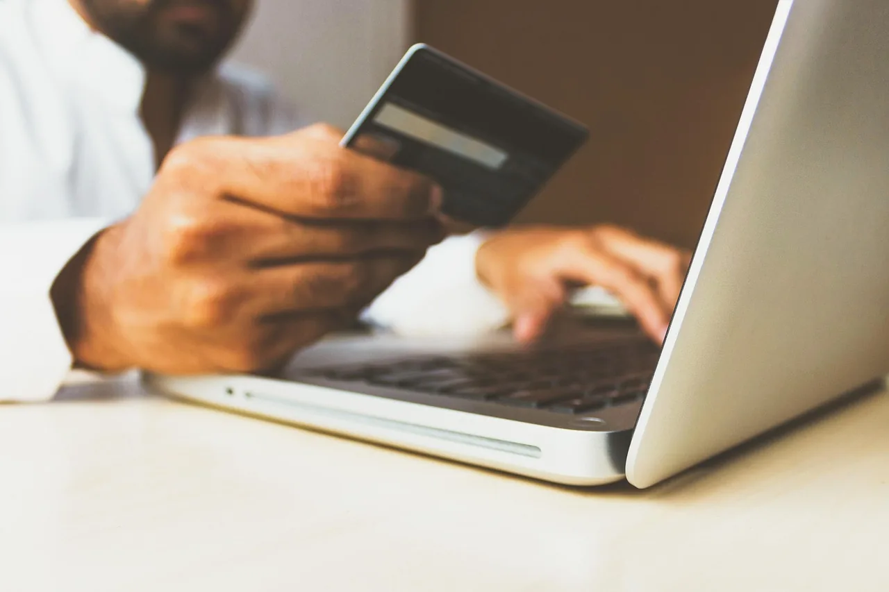 A person holds a card beside an open laptop. No account number is readable.