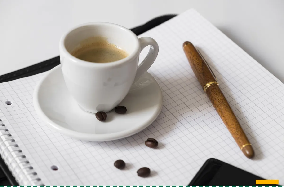 A cup of coffee and a pen on an open grid notebook