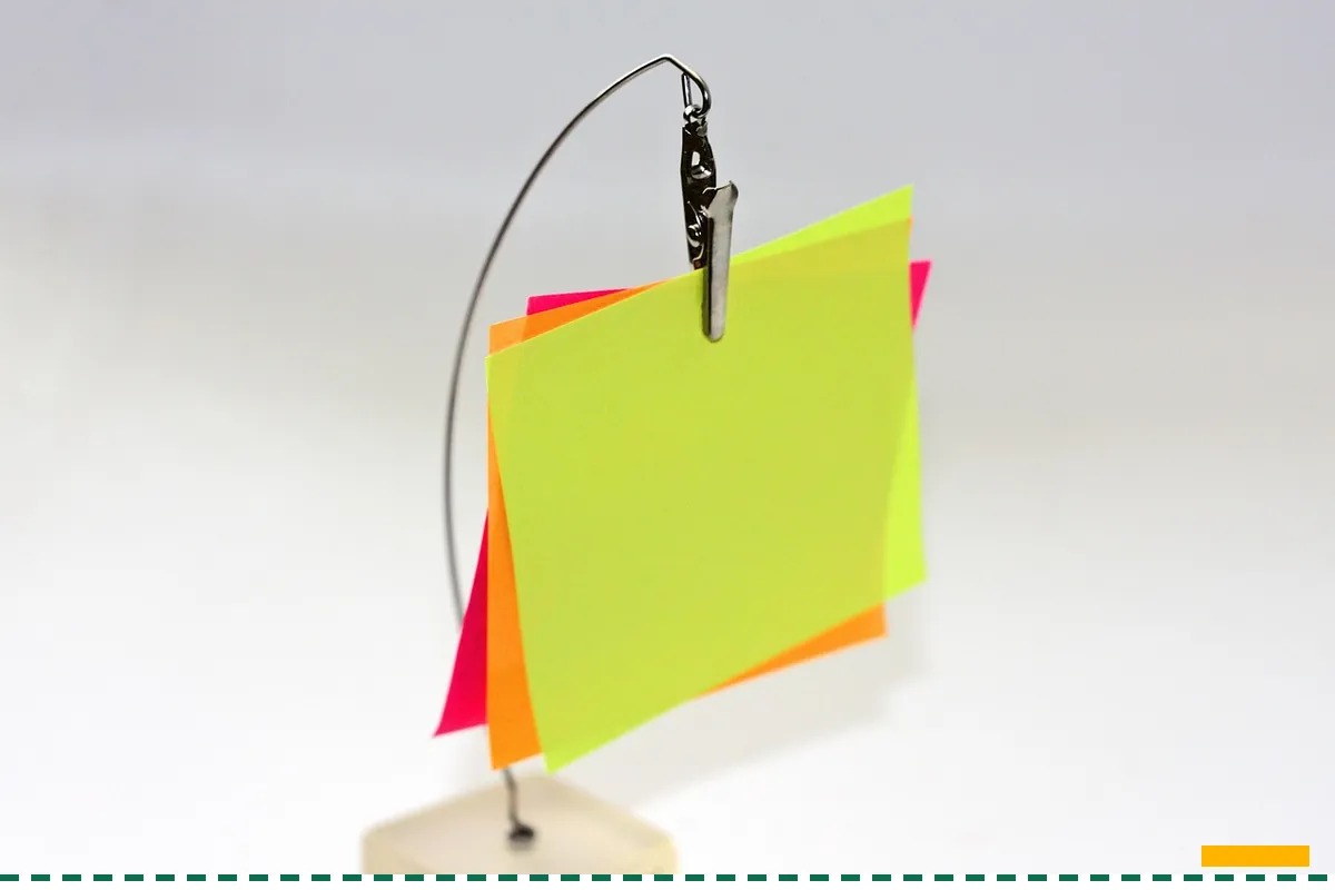 A small stack of sticky notes held up by a wire clip