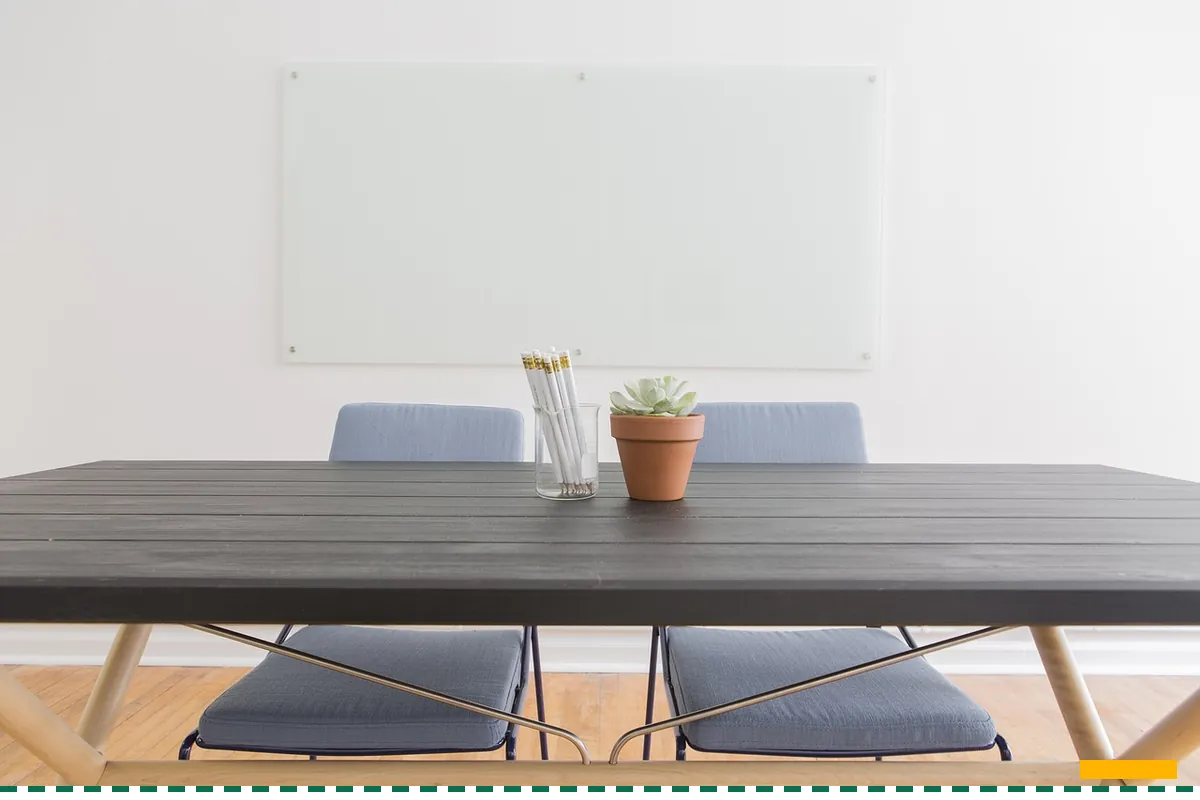 An empty meeting table with two chairs pulled in and a blank whiteboard behind