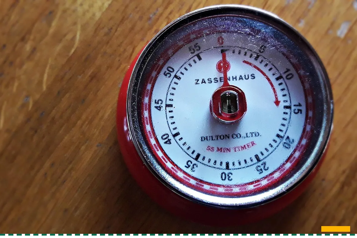 A red kitchen timer on a wooden table