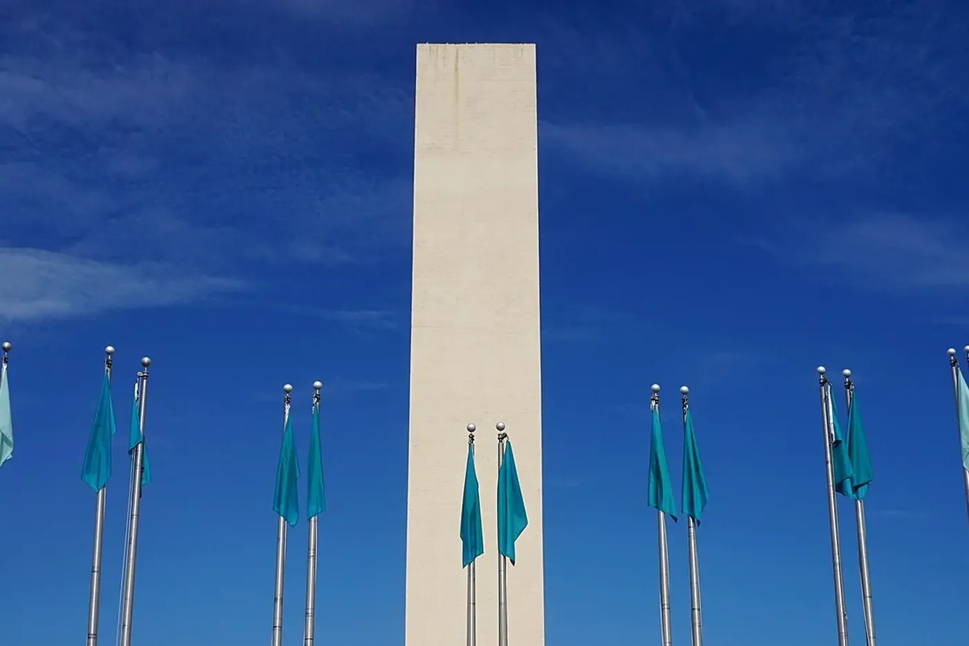 The Fair Park gate in Dallas, a tall pale pylon and rows of flagpoles under a blue sky.