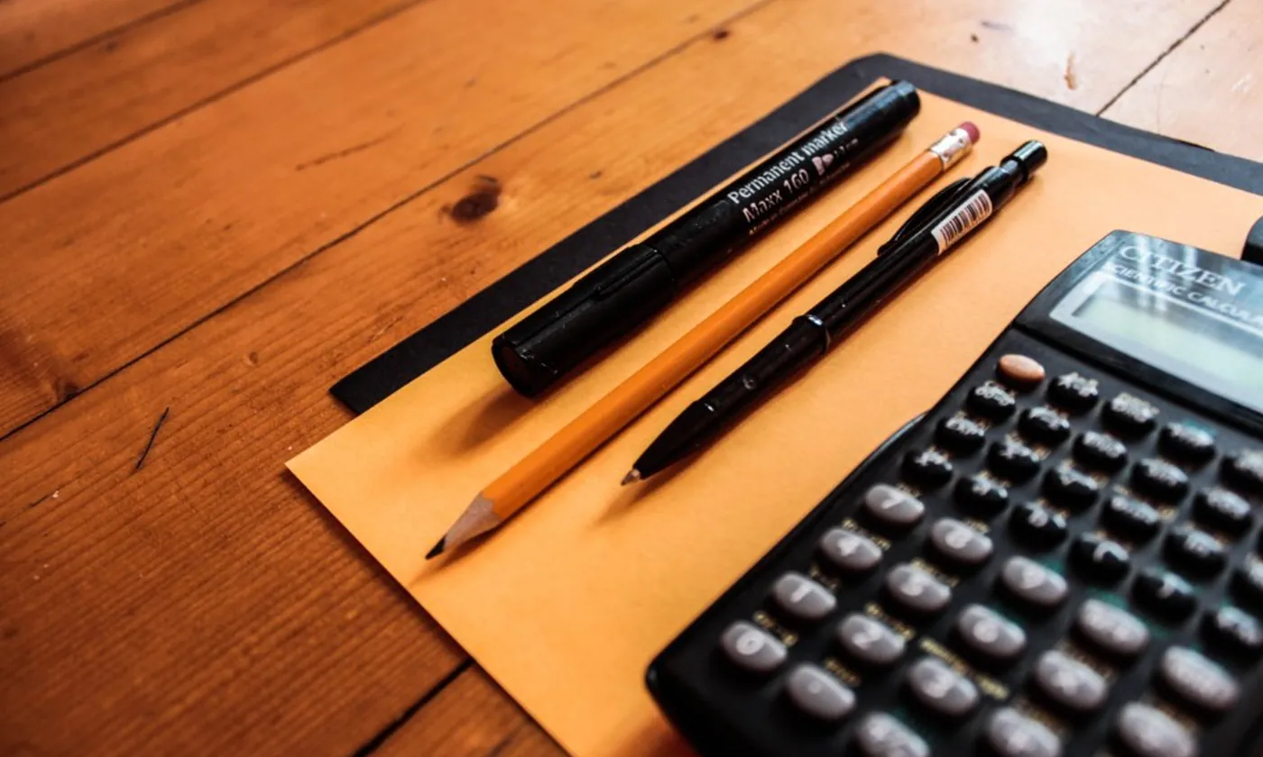 A calculator, pencils and a pen on a paper folder on a wooden table