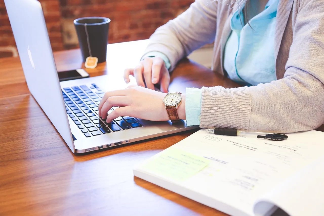 Hands on a laptop beside a printed form and a pen