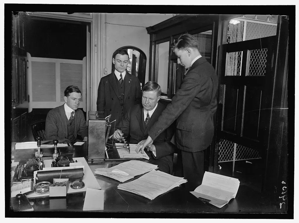 Treasury staff at a check signing machine with stacks of paper