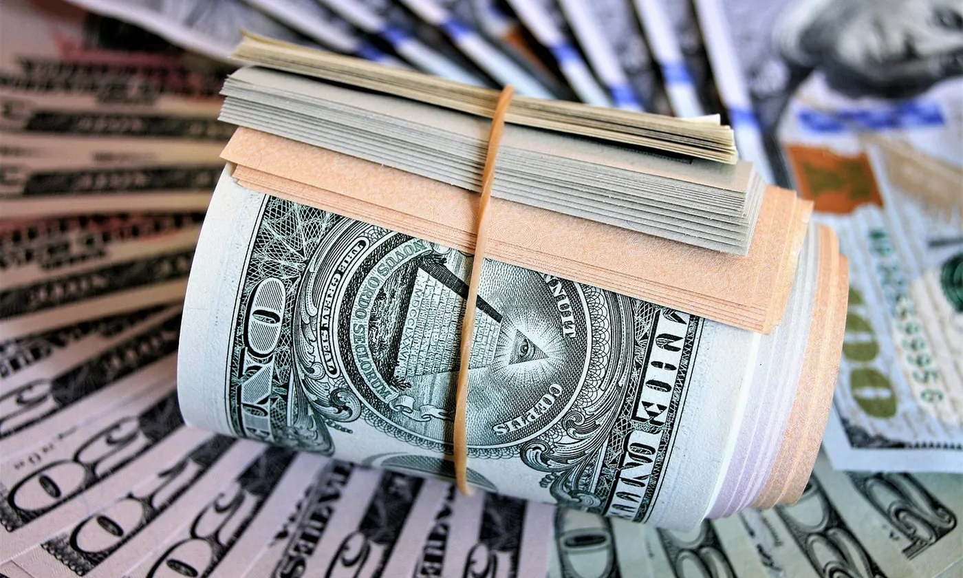 A roll of United States bills lying on a fan of currency