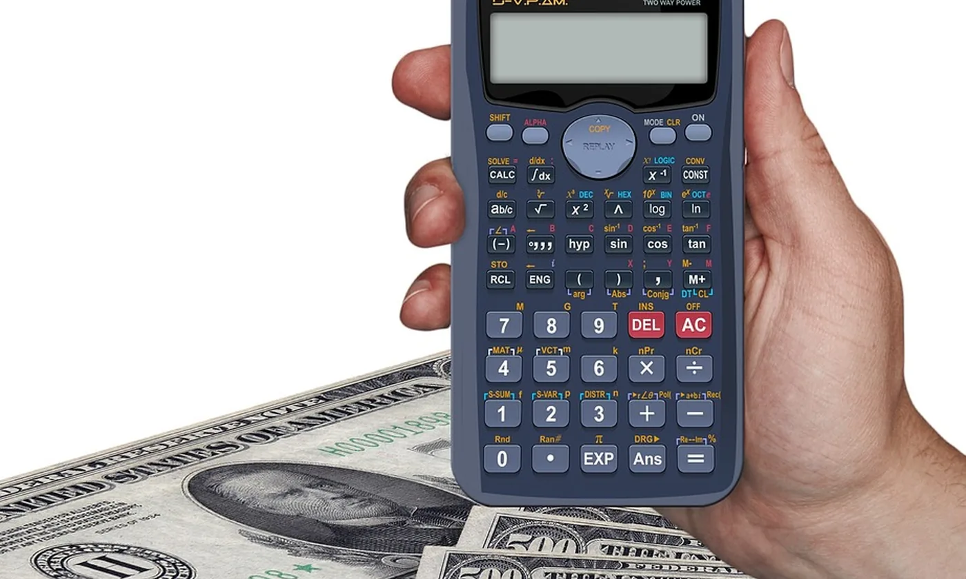 A hand holding a calculator over United States bills