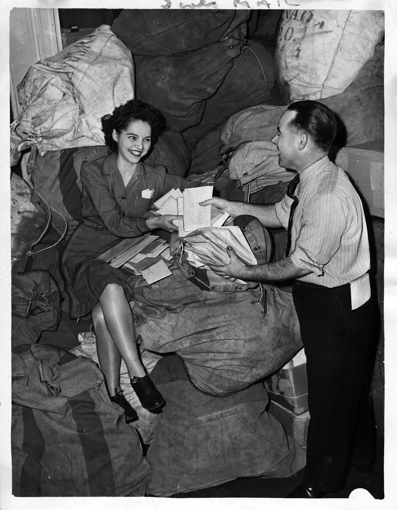Two people hand a stack of returns across a pile of mail sacks, each holding papers the other is about to take