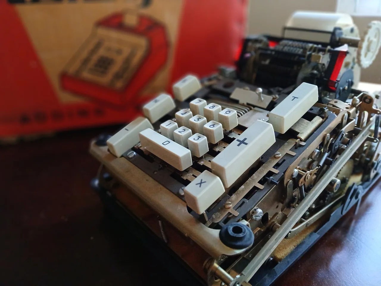 An open adding machine with number keys and a paper tape, the cover off so the works show