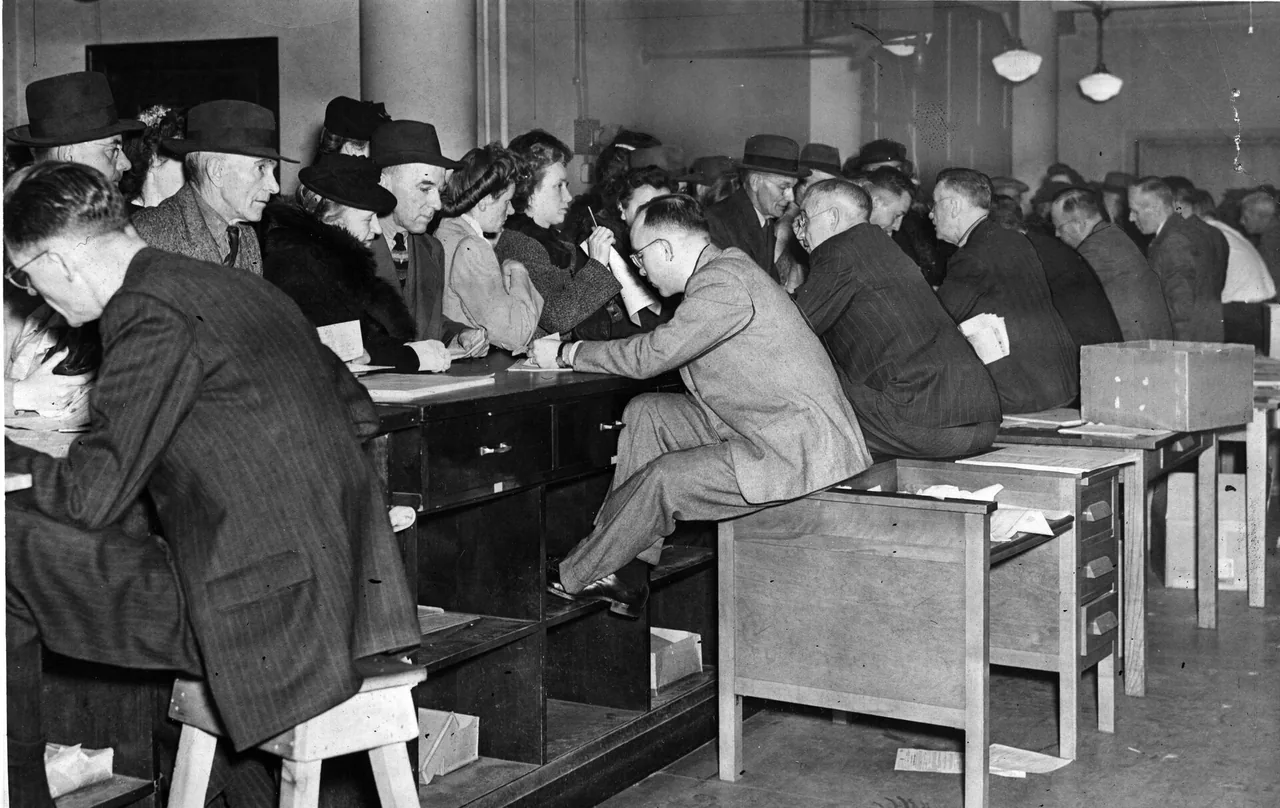 Clerks lean across a long counter while customers sit with papers, the room full of returns being walked through