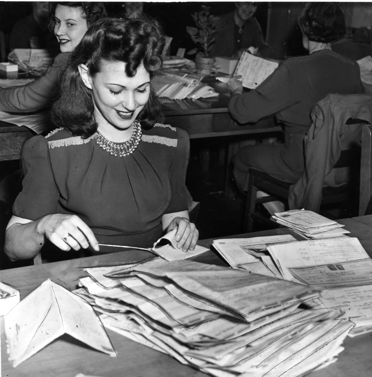 A woman opens a mailed return at a table already covered with envelopes and filed sheets