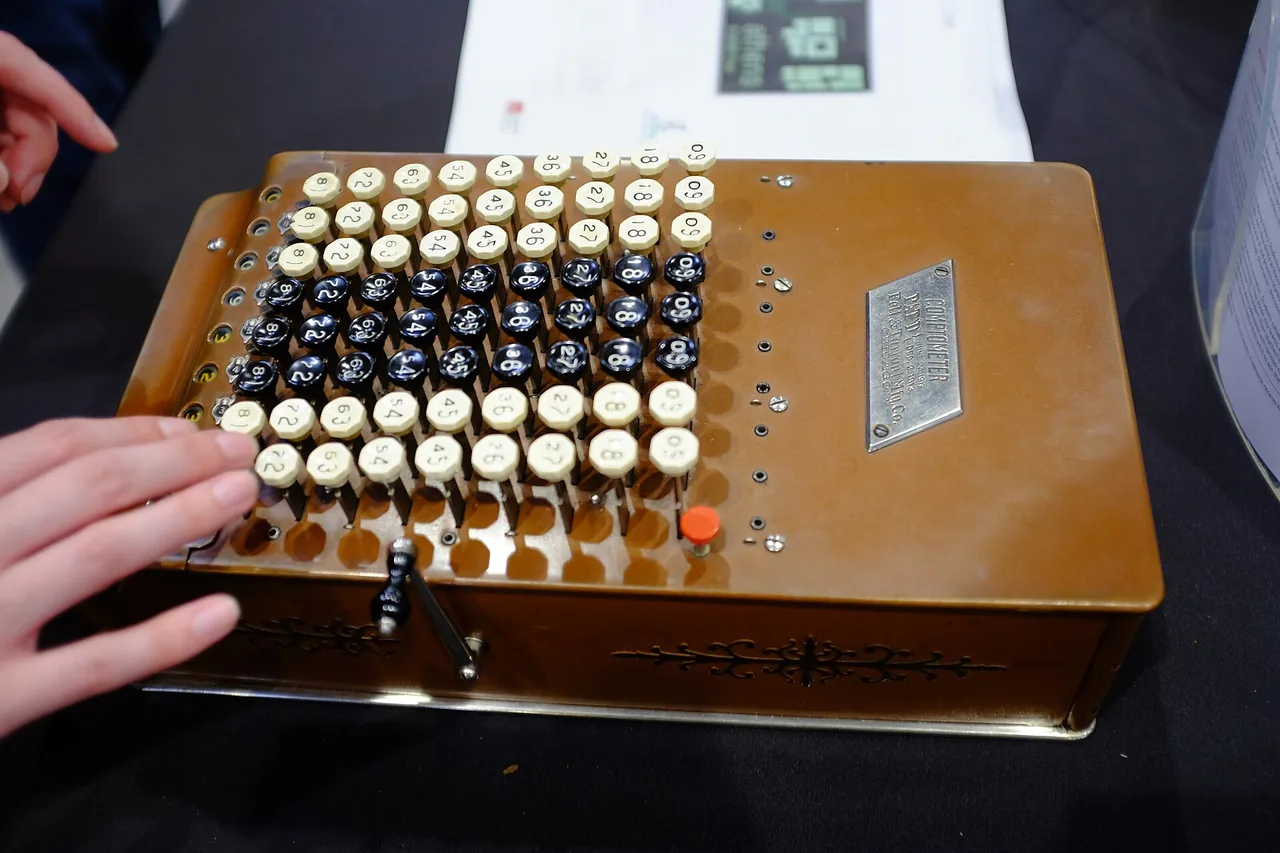 Hands rest beside a comptometer keypad, the keys numbered and ready for a total