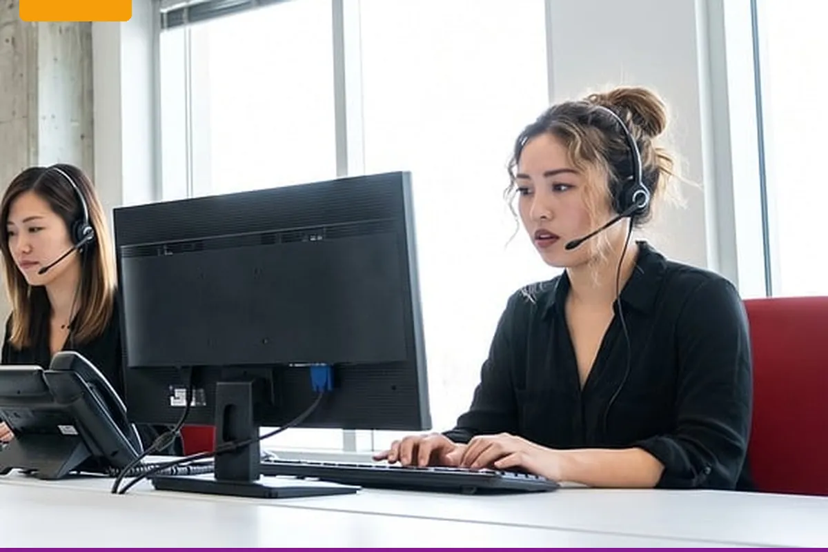Two people at a desk wearing headsets, with the monitor backs toward the camera