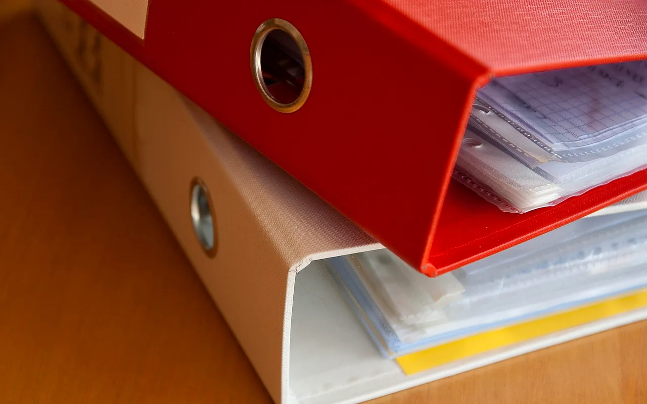 Two binders of sleeved pages stacked on a wooden table, graph paper showing at the edge.
